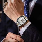 A man in a business suit adjusts his cuff while wearing the POEDAGAR 866 luxury square wristwatch with a silver and gold-tone band.