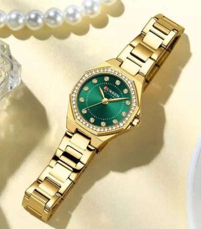 A CURREN 9100 Lady watch with a gold-tone band and a sparkling green dial, placed on a light-colored surface with pearls.