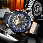 CURREN 8380 chronograph men's watch with a blue dial, rose gold case, and black leather strap resting on a dark surface.