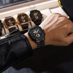 A man wearing the black Poedagar 628 minimalist watch with a matching stainless steel strap, with other watches in the background.