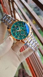 A close-up view of the POEDAGAR 973 luxury watch for men, held by a gloved hand, showing its green dial and two-tone band.