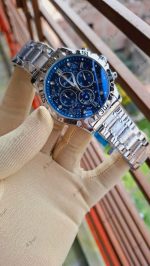 A gloved hand holding the POEDAGAR 973 luxury sports watch, which has a silver metal band and a detailed blue dial.