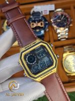 A gloved hand holding a Casio AE-1200WHL-5AV men's watch with a gold-colored case and a brown leather strap.
