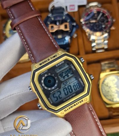 A gloved hand holding a Casio AE-1200WHL-5AV men's watch with a gold-colored case and a brown leather strap.