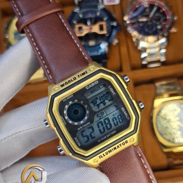 A gloved hand holding a Casio AE-1200WHL-5AV men's watch with a gold-colored case and a brown leather strap.