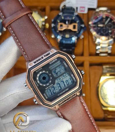 A gloved hand holding a Casio AE-1200WHL-5AV men's watch. The watch has a rose gold case and a brown leather strap.