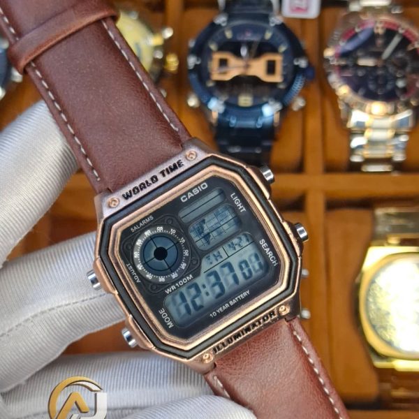 A gloved hand holding a Casio AE-1200WHL-5AV men's watch. The watch has a rose gold case and a brown leather strap.