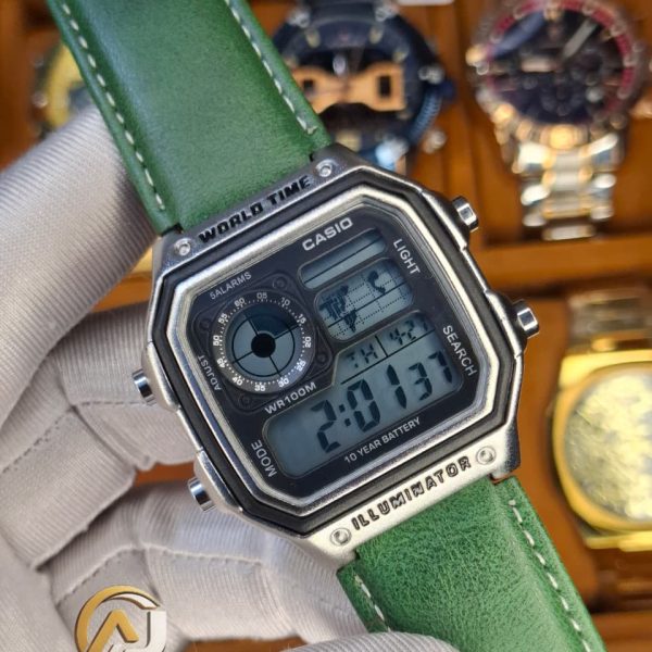 A person wearing a white glove holding a Casio AE-1200WHL-5AV men's watch with a distinctive green leather strap.