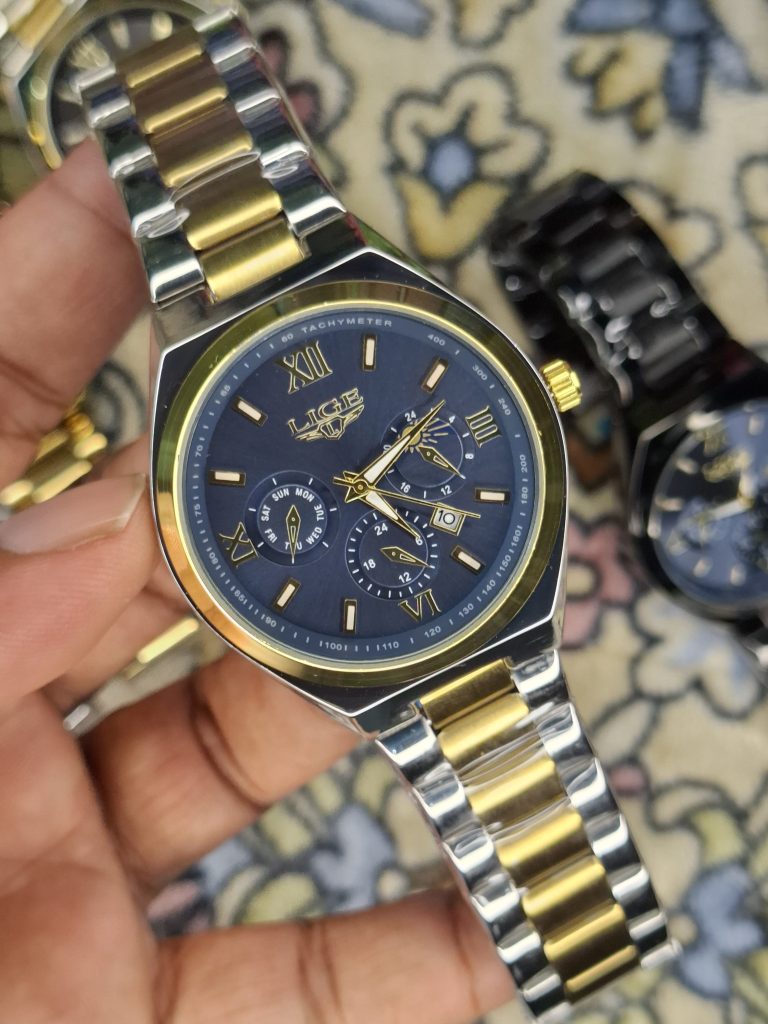 A close-up, top-down shot of a gold-toned LIGE luxury chronograph watch being held by a hand
