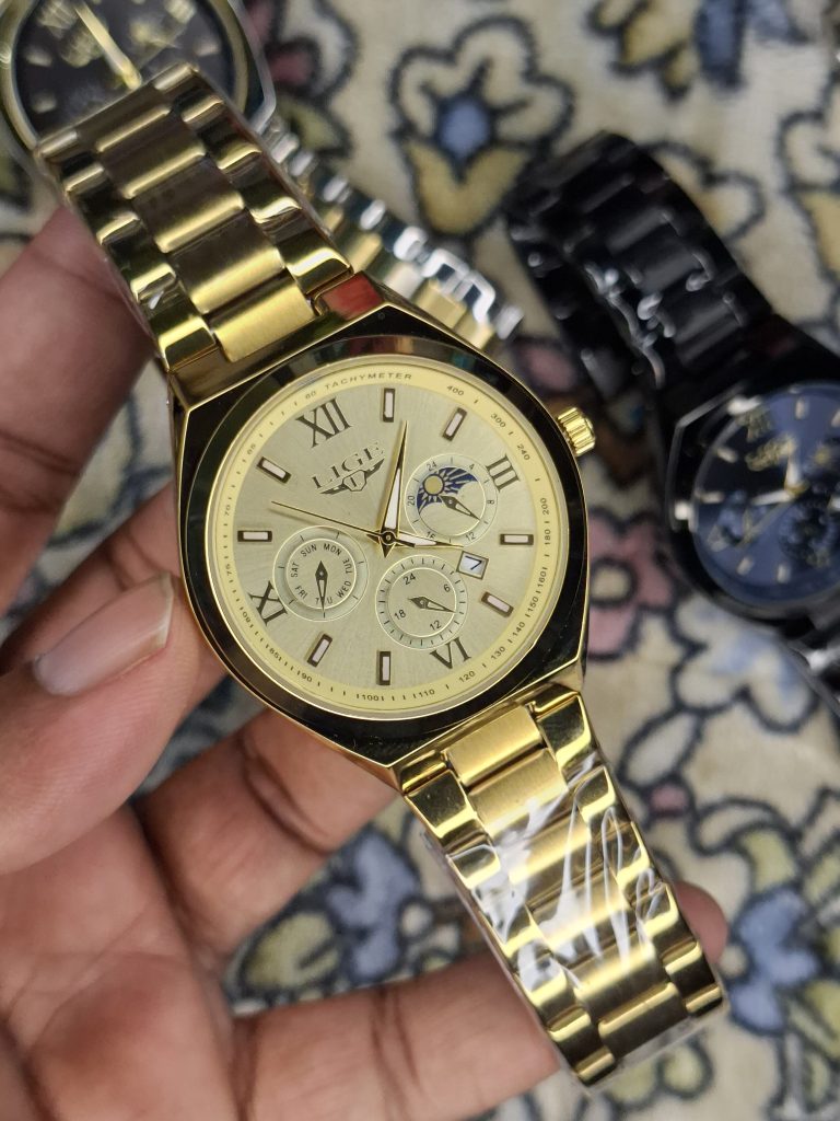 A close-up, top-down shot of a gold-toned LIGE luxury chronograph watch being held by a hand
