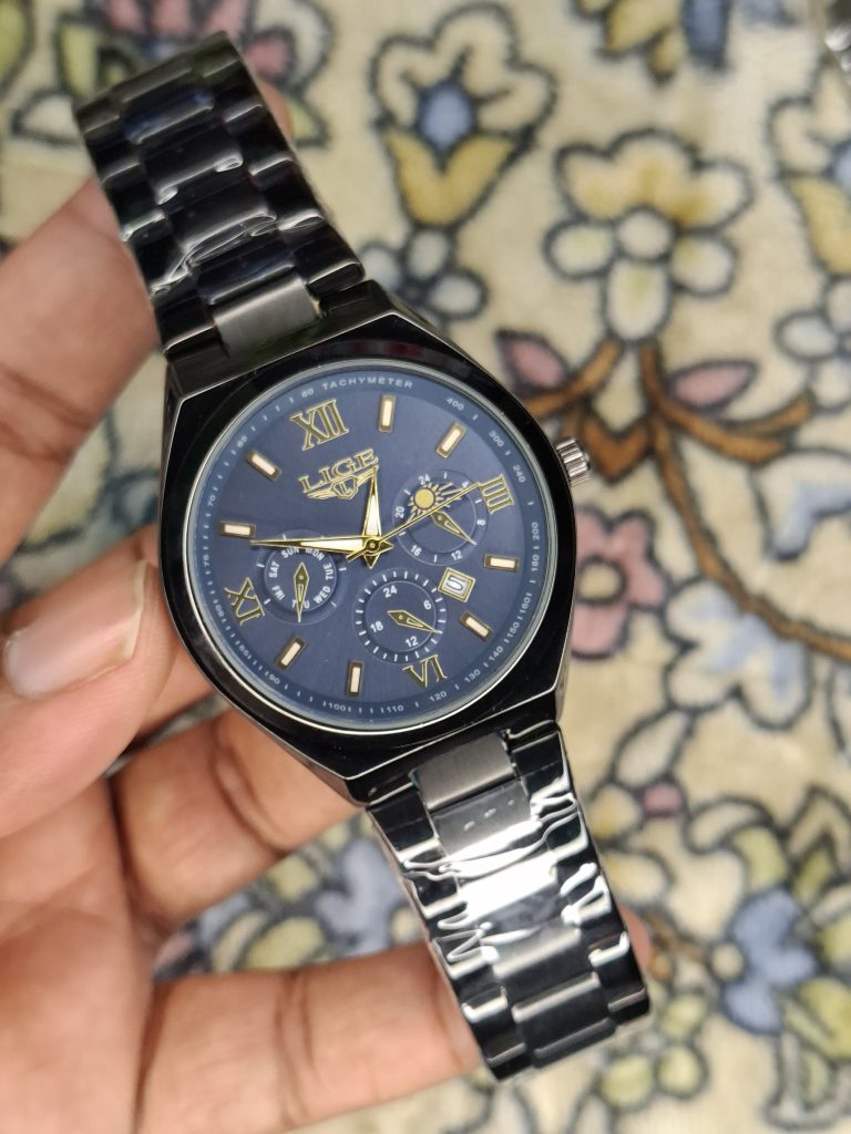 A close-up, top-down shot of a gold-toned LIGE luxury chronograph watch being held by a hand