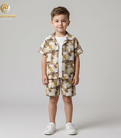 A young boy smiling and posing in a coordinated two-piece summer outfit. He is wearing a short-sleeved, button-down shirt with a Cuban collar and matching shorts, both featuring a light grey-green floral and botanical print on an ecru background. He is also wearing white socks and white sneakers, standing against a plain grey backdrop.